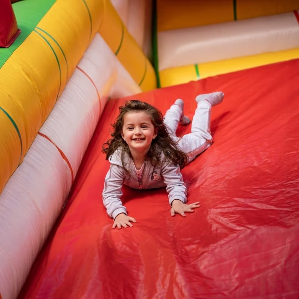 Menina sorrindo ao descer de barriga um tobogã inflável vermelho